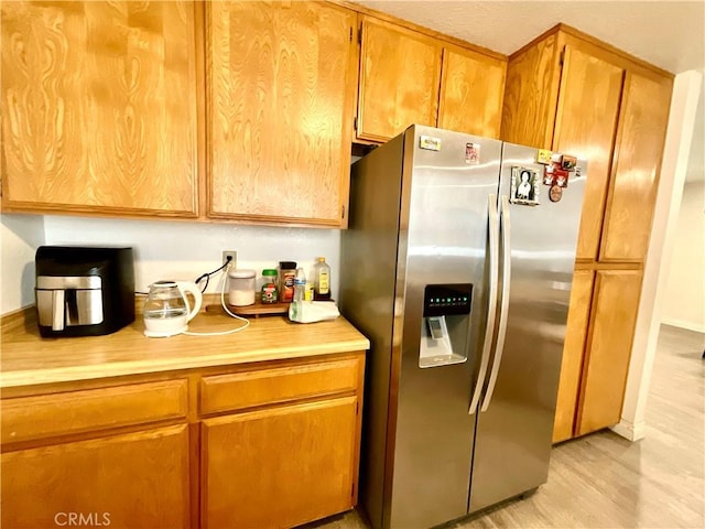 1078 W King St, Banning, CA 92220 - kitchen featuring brown cabinetry, baseboards, light wood-style flooring, light countertops, and stainless steel fridge with ice dispenser