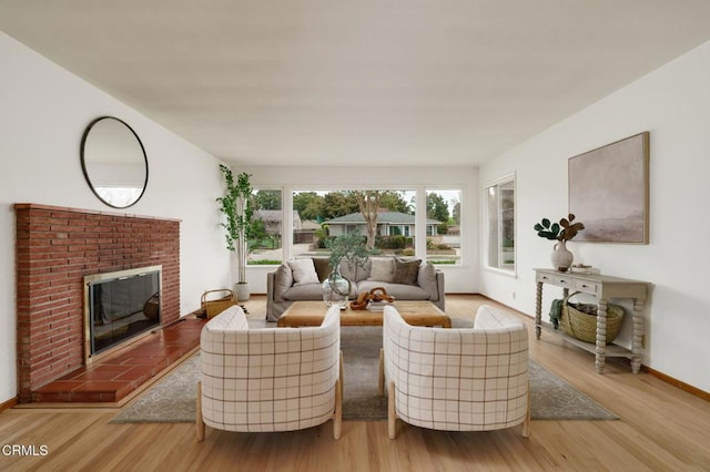 living area with baseboards, a brick fireplace, and wood finished floors