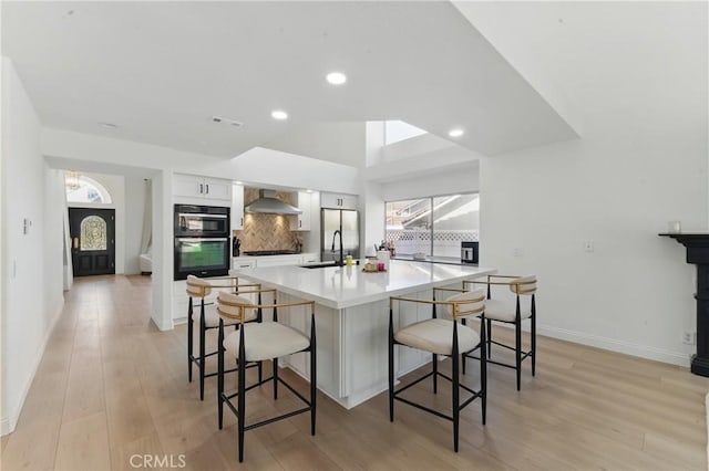 3381 Deaver Dr, Corona, CA 92882 - kitchen featuring white cabinets, wall chimney range hood, a sink, dobule oven black, and a breakfast bar area
