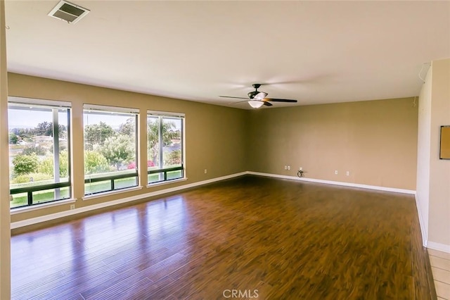 empty room featuring baseboards, visible vents, dark wood-style floors, and ceiling fan