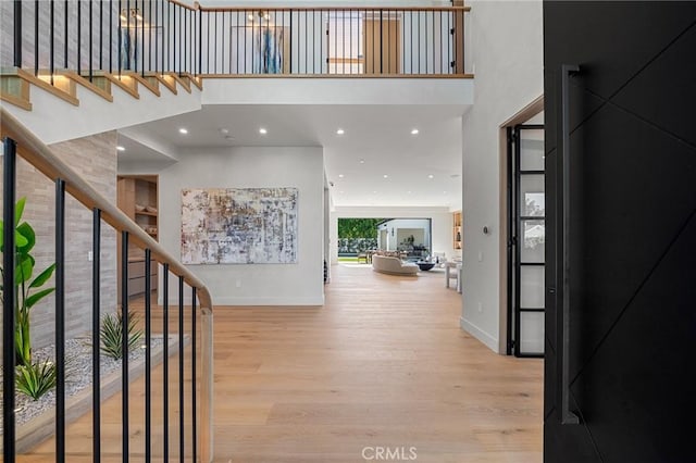 foyer entrance featuring baseboards, a high ceiling, stairs, and light wood-style flooring