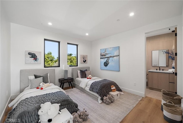 bedroom featuring recessed lighting, a sink, light wood-style floors, baseboards, and ensuite bathroom