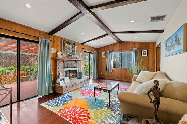 living area featuring visible vents, wood walls, wood finished floors, a fireplace, and lofted ceiling with beams
