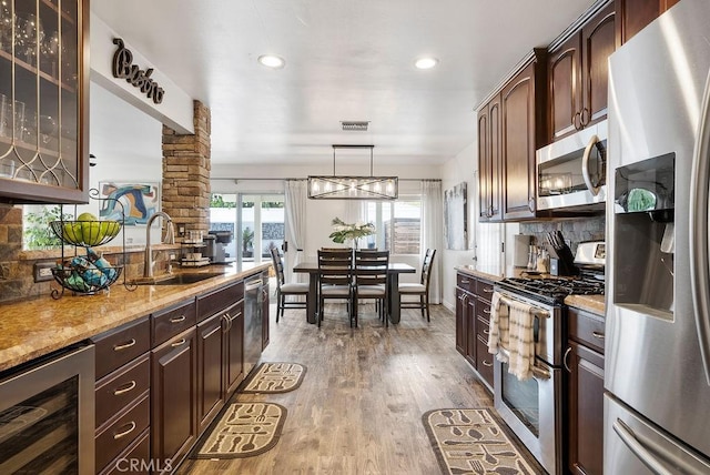 kitchen with glass insert cabinets, beverage cooler, a sink, light wood finished floors, and stainless steel appliances