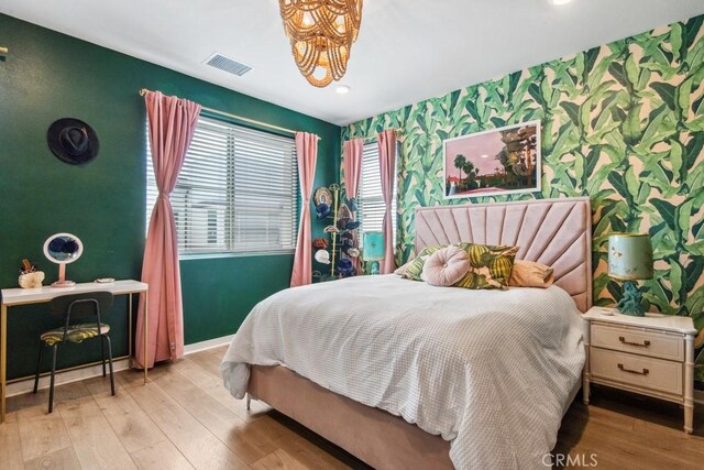 bedroom with wallpapered walls, wood finished floors, visible vents, an accent wall, and baseboards