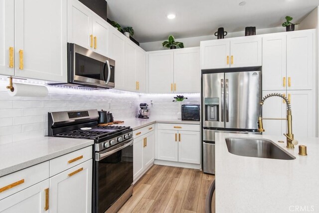 kitchen with stainless steel appliances, light countertops, a sink, light wood-style flooring, and white cabinetry