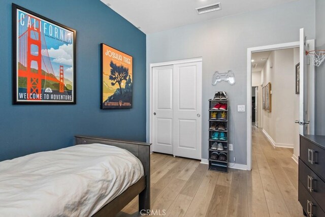bedroom featuring light wood-type flooring, baseboards, visible vents, and a closet