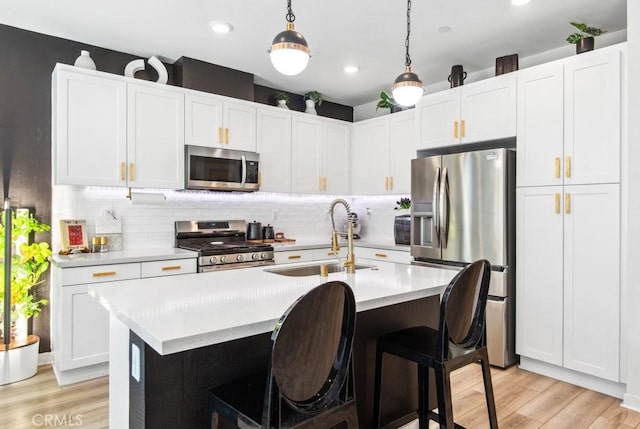 kitchen with a sink, light wood-type flooring, a center island with sink, light countertops, and appliances with stainless steel finishes