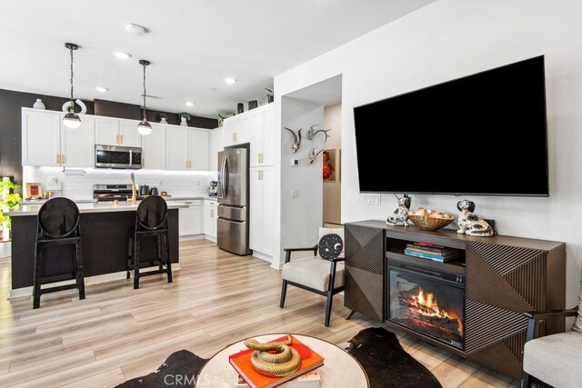 living area featuring light wood-style flooring, a glass covered fireplace, and recessed lighting