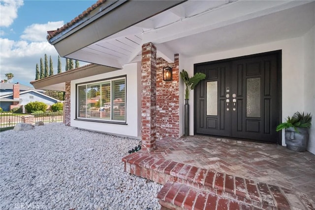 view of exterior entry with stucco siding and fence