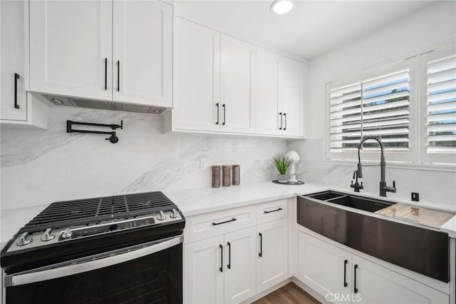 kitchen featuring white cabinets, stainless steel range with gas stovetop, under cabinet range hood, and a sink