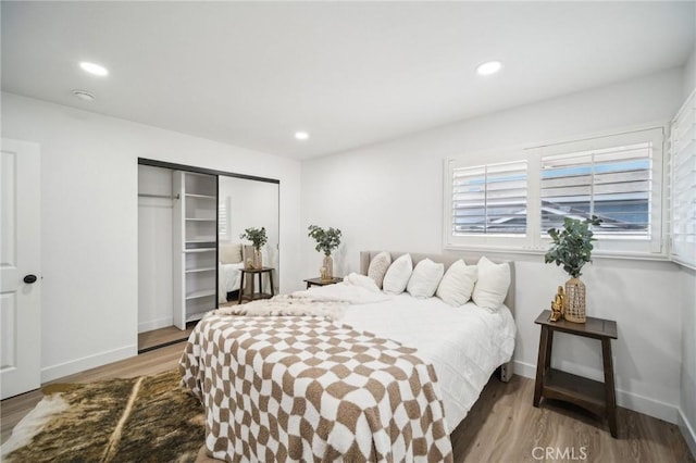 bedroom featuring baseboards, wood finished floors, recessed lighting, and a closet