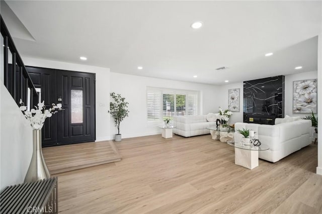 living room featuring light wood-style flooring, visible vents, baseboards, recessed lighting, and stairs