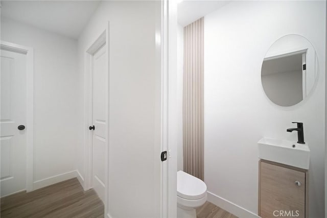 bathroom with baseboards, wood finished floors, vanity, and toilet