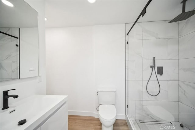 bathroom featuring a tile shower, toilet, baseboards, wood finished floors, and vanity