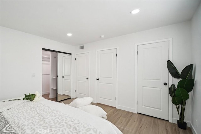 bedroom featuring baseboards, wood finished floors, visible vents, and two closets