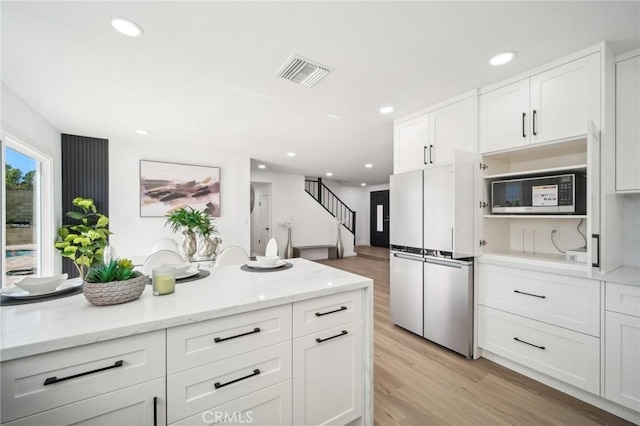 kitchen featuring built in microwave, white cabinets, visible vents, freestanding refrigerator, and light wood-style flooring
