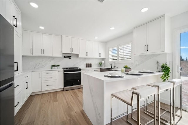 kitchen featuring light wood finished floors, a sink, appliances with stainless steel finishes, light countertops, and a breakfast bar area