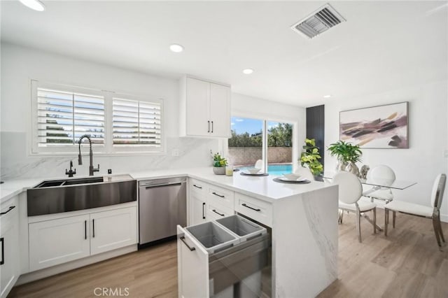 kitchen with stainless steel dishwasher, a sink, light wood finished floors, white cabinets, and visible vents