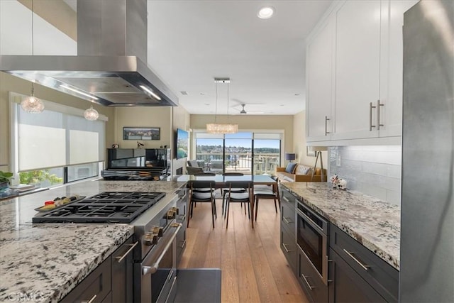 kitchen with white cabinets, stainless steel appliances, island range hood, light wood-type flooring, and light stone countertops