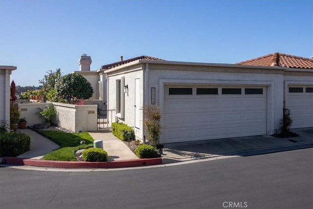 view of front of property featuring a garage, a tile roof, a chimney, and stucco siding
