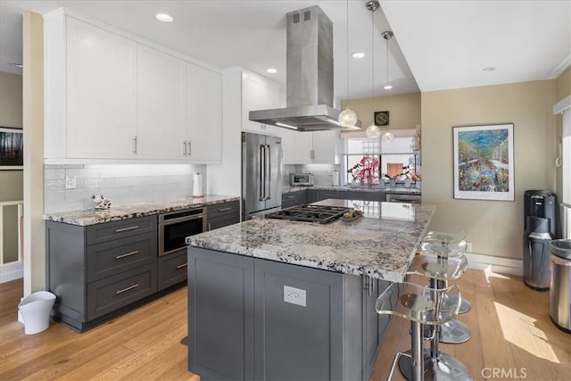 kitchen with light wood finished floors, island exhaust hood, white cabinets, and appliances with stainless steel finishes