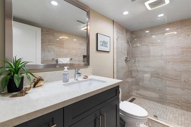 bathroom with a tile shower, toilet, vanity, and visible vents