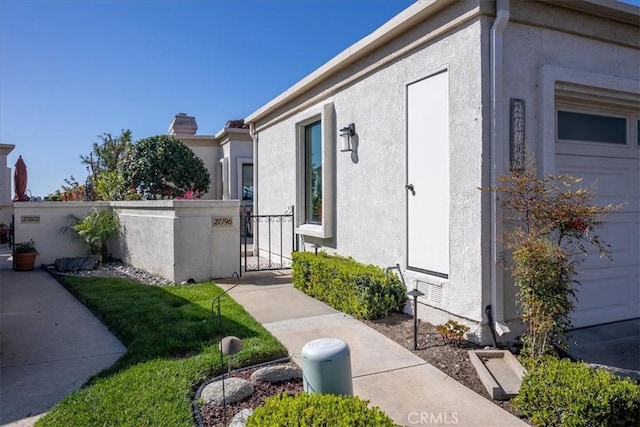view of side of home with fence, a chimney, a gate, and stucco siding