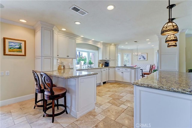 kitchen featuring visible vents, white cabinets, a peninsula, stone tile flooring, and a notable chandelier