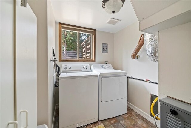 clothes washing area with laundry area, stone finish flooring, visible vents, baseboards, and washer and clothes dryer