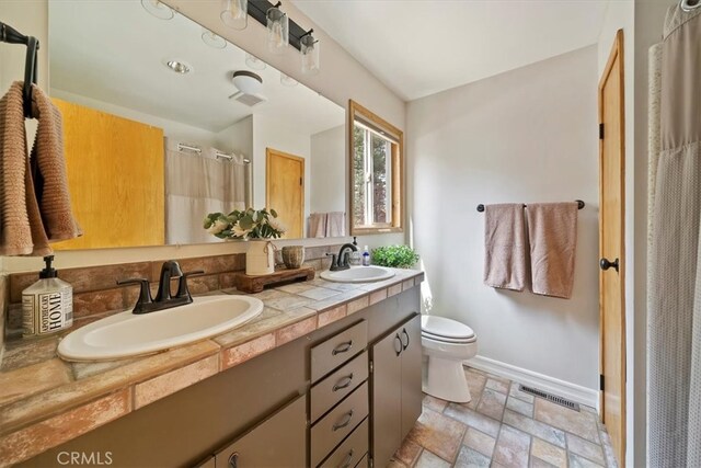 bathroom with visible vents, a sink, baseboards, and stone finish floor