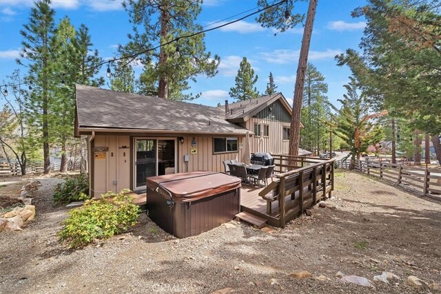 back of house featuring board and batten siding, a deck, a hot tub, fence, and a shingled roof