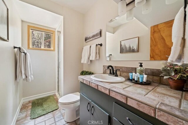 bathroom with vanity, toilet, stone finish floor, baseboards, and a stall shower