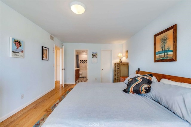 bedroom featuring baseboards, light wood finished floors, ensuite bath, and visible vents