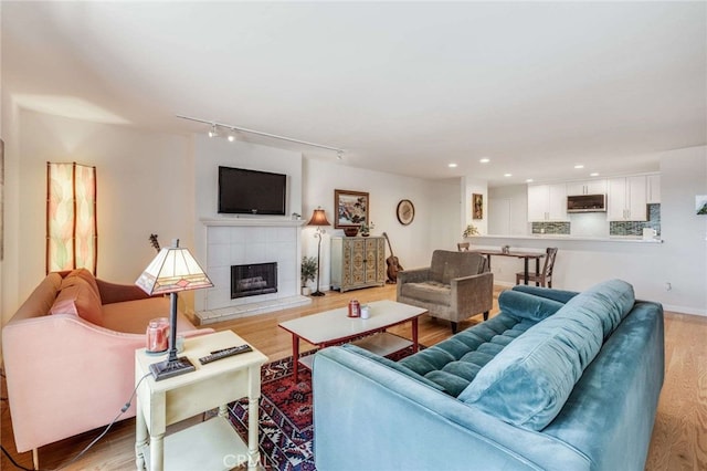 living area featuring recessed lighting, track lighting, a tiled fireplace, and light wood-type flooring
