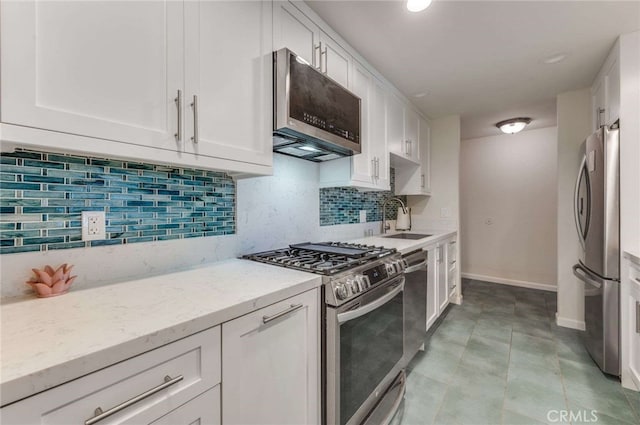 kitchen featuring appliances with stainless steel finishes, light stone countertops, a sink, baseboards, and white cabinetry