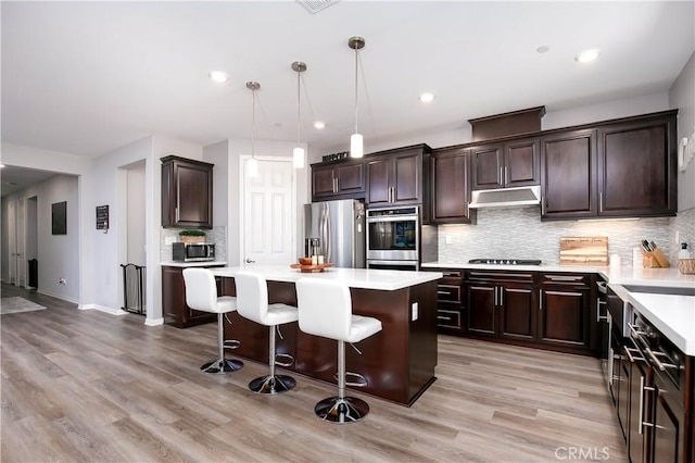 6335 Oldfield St, Lancaster, CA 93536 - kitchen featuring appliances with stainless steel finishes, under cabinet range hood, a kitchen island, a breakfast bar, and light countertops