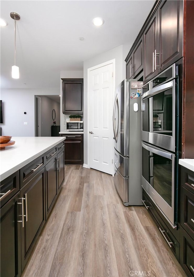 6335 Oldfield St, Lancaster, CA 93536 - kitchen featuring appliances with stainless steel finishes, light countertops, light wood-style flooring, hanging light fixtures, and dark brown cabinets