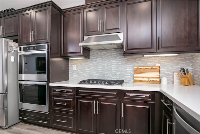 6335 Oldfield St, Lancaster, CA 93536 - kitchen with appliances with stainless steel finishes, range hood, light countertops, light wood-style floors, and dark brown cabinets