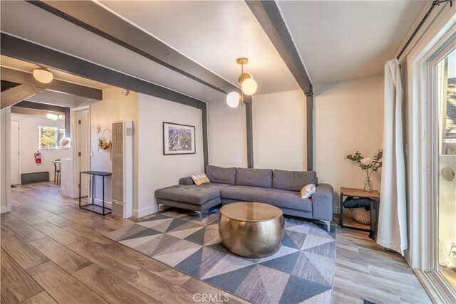 living area with baseboards, a heating unit, beam ceiling, and light wood-style flooring