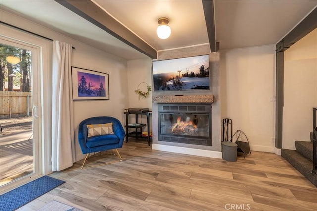 sitting room with beam ceiling, baseboards, a glass covered fireplace, wood finished floors, and stairway