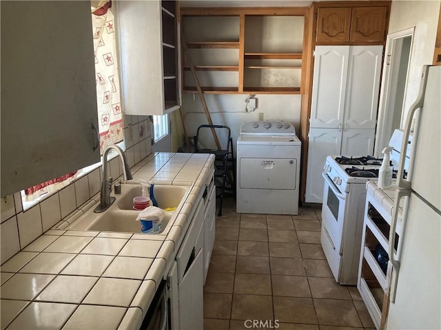 kitchen with a sink, white appliances, open shelves, tile counters, and washer / dryer