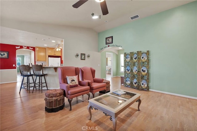 living area with arched walkways, baseboards, light wood-style floors, a ceiling fan, and high vaulted ceiling