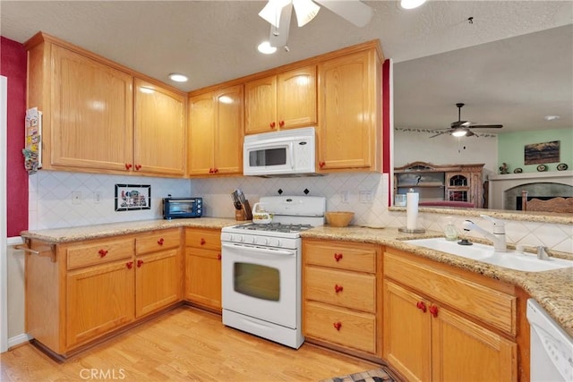 kitchen featuring light wood finished floors, a ceiling fan, a sink, white appliances, and decorative backsplash