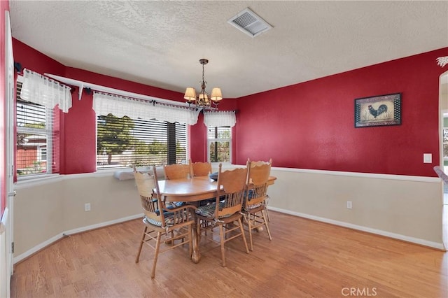 dining space with wood finished floors, a textured ceiling, a chandelier, baseboards, and visible vents