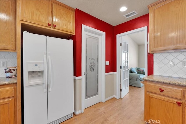 kitchen with backsplash, light wood-type flooring, visible vents, and white refrigerator with ice dispenser