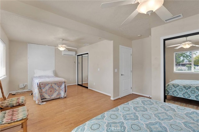 bedroom with an AC wall unit, visible vents, baseboards, a ceiling fan, and wood finished floors