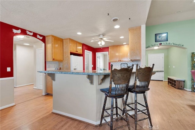 kitchen featuring white fridge with ice dispenser, light wood-type flooring, ceiling fan, arched walkways, and backsplash