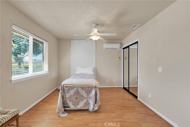 bedroom featuring a wall mounted air conditioner, a closet, light wood-type flooring, baseboards, and visible vents