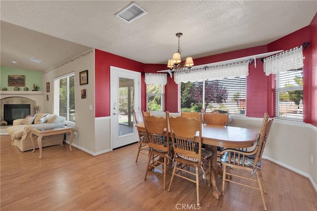 dining area featuring light wood finished floors, visible vents, a textured ceiling, and a notable chandelier
